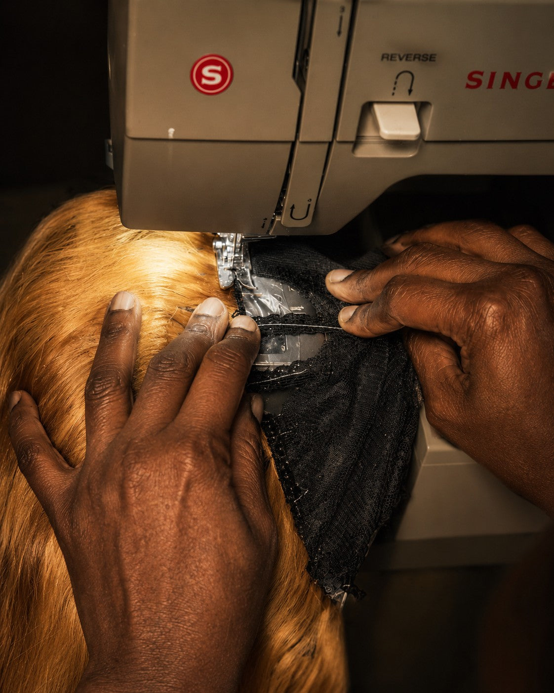 Mary's hands guiding a black lace cap and blonde hair under the needle of a Singer sewing machine